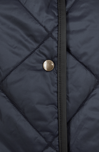 Detailansicht des Damen-Steppmantels Luisa-QS von Frauenschuh in der Farbe Midnight (dunkelblau). Abgebildet ist ein einzelner Druckknopf, die fein strukturierte Steppung, präzise gesetzte Nähte sowie das glatte, leicht glänzende Material. Die Aufnahme zeigt die hohe Verarbeitungsqualität und das edle Finish des Mantels, ideal für die Übergangszeit im Frühling und Sommer. Der dezente Farbton „Midnight“ unterstreicht den eleganten, zeitlosen Charakter des Designs
