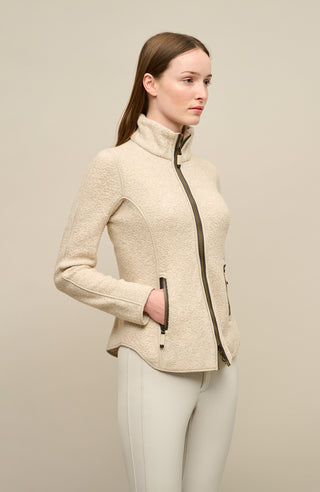 Seitenansicht der Damenjacke „WERA-CT“ in der Farbe „Caramel“, einem Beigeton. Die sportlich-elegante Teddyjacke besteht aus luxuriösem Fleece mit Kaschmiranteil, das besonders weich, wärmend und hochwertig wirkt. Der Schnitt ist modern und leicht tailliert, an den Seiten leicht höher geschnitten um die feminine Silhouette zu betonen, mit einem Stehkragen, durchgehendem Zwei-Wege-Reißverschluss und zwei seitlichen Eingrifftaschen. Wird von einem Model getragen