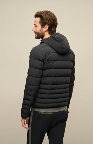 Frauenschuh Herren Daunen-Winterjacke Lorenzo in Schwarz, getragen von einem Model – Rückansicht der stilvollen Funktionsjacke mit gleichmäßigem Steppdesign, fester Kapuze und Zwei-Wege-Zipper. Die Jacke zeigt sich in moderner Optik, ideal für kalte Wintertage und vielseitige Aktivitäten. Warm, leicht und funktional.