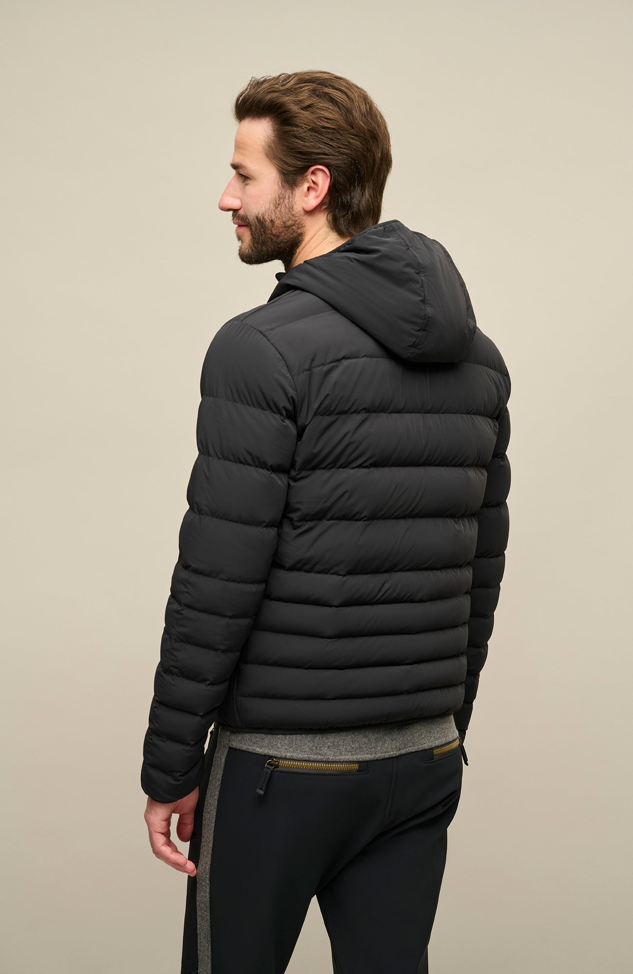 Frauenschuh Herren Daunen-Winterjacke Lorenzo in Schwarz, getragen von einem Model – Rückansicht der stilvollen Funktionsjacke mit gleichmäßigem Steppdesign, fester Kapuze und Zwei-Wege-Zipper. Die Jacke zeigt sich in moderner Optik, ideal für kalte Wintertage und vielseitige Aktivitäten. Warm, leicht und funktional.