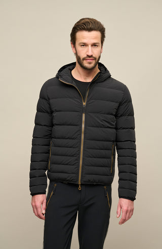 Frauenschuh Herren Daunen-Winterjacke Lorenzo in Schwarz, getragen von einem Model – stilvolle Funktionsjacke mit gleichmäßigem Steppdesign, fester Kapuze und Zwei-Wege-Zipper. Mit zwei seitlichen Reißverschlusstaschen und zwei Innenfächern mit nahtfeinem Zip. Warm, leicht und anschmiegsam für optimale Winterleistung bei gleichzeitig modernem Schnitt und Funktionalität.