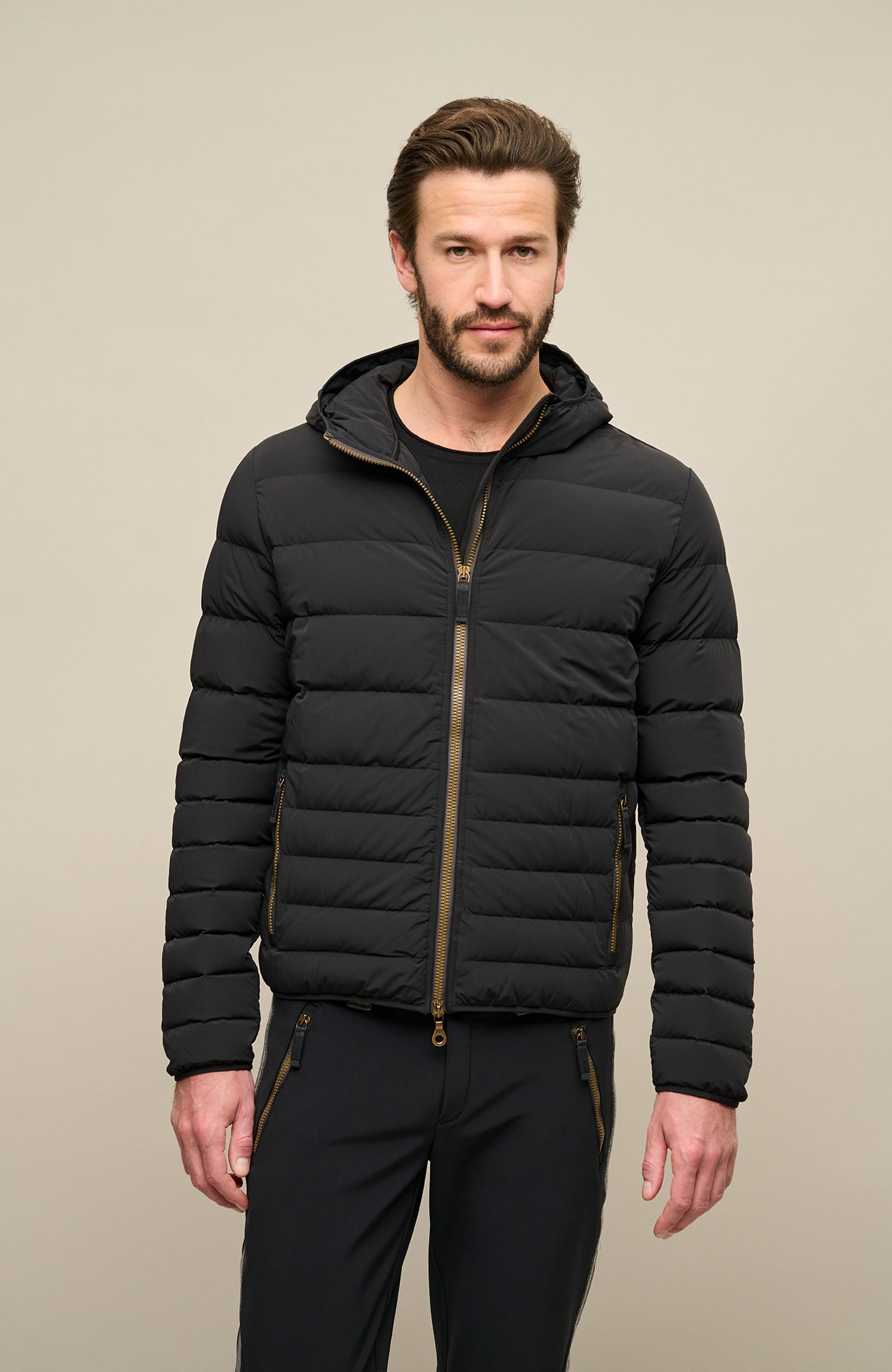 Frauenschuh Herren Daunen-Winterjacke Lorenzo in Schwarz, getragen von einem Model – stilvolle Funktionsjacke mit gleichmäßigem Steppdesign, fester Kapuze und Zwei-Wege-Zipper. Mit zwei seitlichen Reißverschlusstaschen und zwei Innenfächern mit nahtfeinem Zip. Warm, leicht und anschmiegsam für optimale Winterleistung bei gleichzeitig modernem Schnitt und Funktionalität.