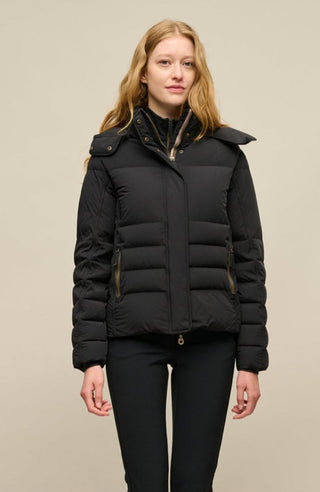 Vorderansicht der Frauenschuh Damen-Daunenjacke Matilde in Schwarz die von einem Model getragen wird– elegante Winterjacke mit hochwertiger Daunenfüllung, gerader Schnitt, verschließbaren Seitentaschen, wasserabweisendes Material, Feuchtigkeitsregulierend und Kapuze die man abnehmen kann, ideal für kalte Wintertage. Die Jacke kann mit einem Reißverschluss oder Druckknöpfen verschlossen werden, beides ist vorhanden.