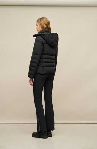 Rückansicht der Frauenschuh Damen-Daunenjacke Matilde in Schwarz die von einem Model getragen wird – elegante Winterjacke mit hochwertiger Daunenfüllung, gerader Schnitt, verschließbaren Seitentaschen, wasserabweisendes Material, Feuchtigkeitsregulierend und Kapuze die man abnehmen kann, ideal für kalte Wintertage. Die Jacke verfügt über einen Reißverschluss und einer Druckknopfleiste um diese zu schließen