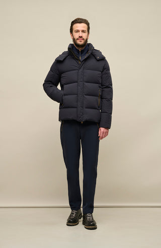 Vorderansicht der Frauenschuh Daunenjacke Mattia für Herren in Dunkelblau die von einem Model getragen wird – warme Winterjacke mit abknöpfbarer und verstellbarer Kapuze, modernem Steppmuster, verschließbaren Seitentaschen und zusätzlicher Knopfleiste. Sie ist außerdem Feuchtigkeitsregulierend, Wasserabweisend, Wärmend, Atmungsaktiv und Elastisch.