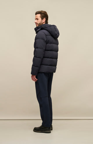 Seitenansicht der Frauenschuh Daunenjacke Mattia für Herren in Dunkelblau die von einem Model getragen wird– warme Winterjacke mit abknöpfbarer und verstellbarer Kapuze, modernem Steppmuster, verschließbaren Seitentaschen und zusätzlicher Knopfleiste. Sie ist außerdem Feuchtigkeitsregulierend, Wasserabweisend, Wärmend, Atmungsaktiv und Elastisch.