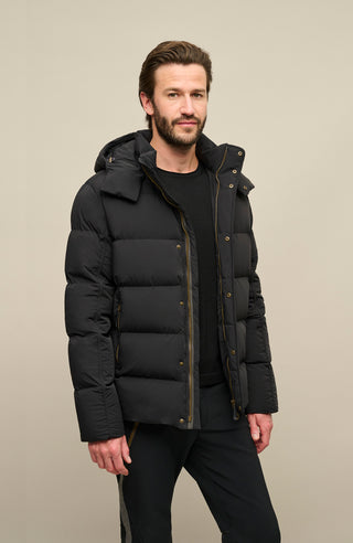 Seitenansicht der Frauenschuh Daunenjacke Mattia für Herren in Schwarz die von einem Model getragen wird– warme Winterjacke mit abknöpfbarer und verstellbarer Kapuze, modernem Steppmuster, verschließbaren Seitentaschen und zusätzlicher Knopfleiste. Sie ist außerdem Feuchtigkeitsregulierend, Wasserabweisend, Wärmend, Atmungsaktiv und Elastisch.