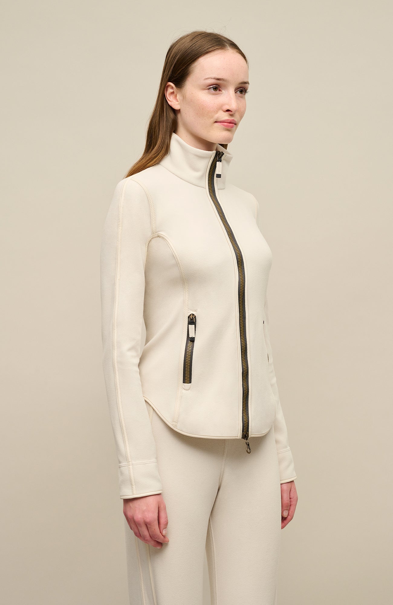 Nachhaltige Damen Fleecejacke in der Farbe Sandstone von Frauenschuh, ideal für alle Jahreszeiten. Modisches Design mit seitlich hoch geschnittenem Schnitt und Zwei-Wege-Reißverschluss für mehr Flexibilität. Modell Wera, Fleecejacke für den komfortablen und stilvollen Alltag. Seitenansicht getragen von einem Model