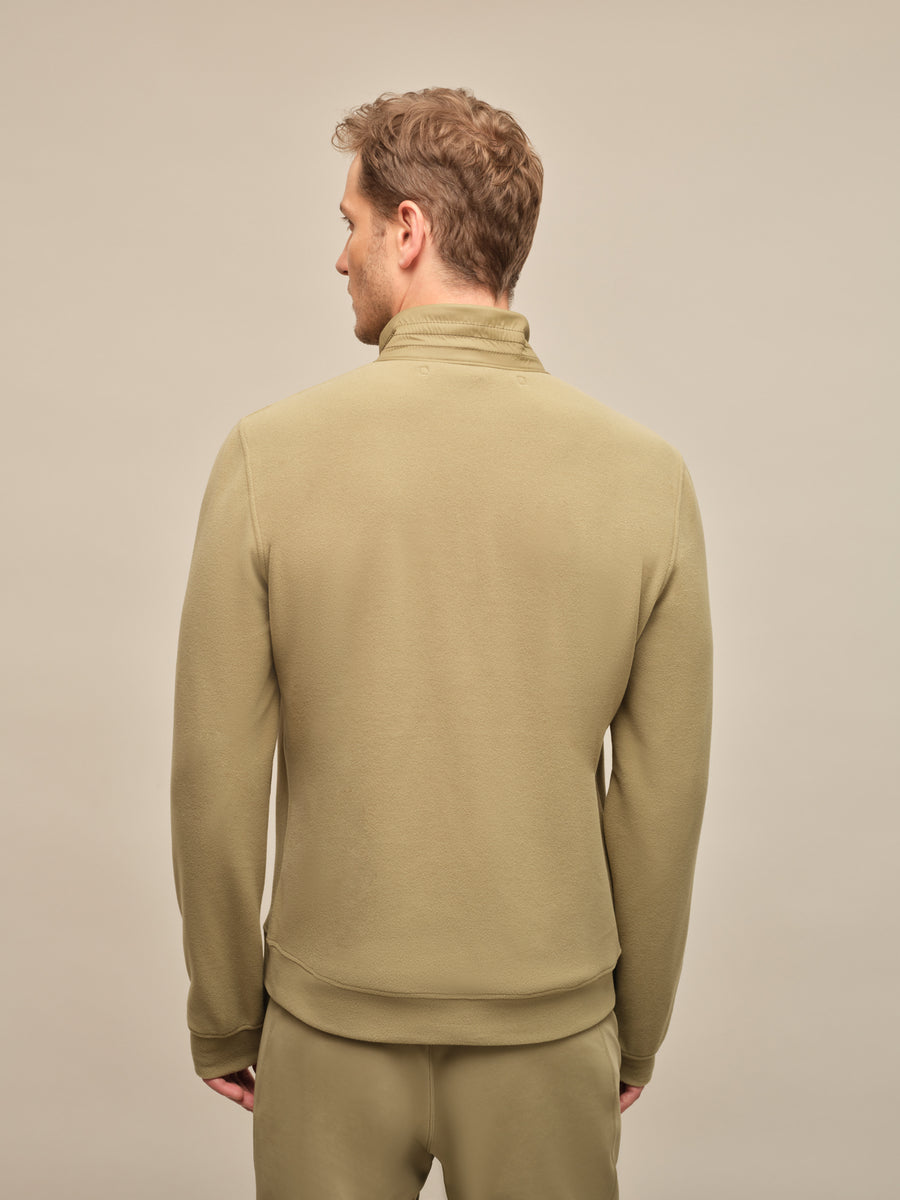 Rückansicht einer Herrenjacke aus der Frühjahrs- und Sommerkollektion von Frauenschuh. Der Rücken ist glatt und schlicht gehalten, mit leicht taillierter Form für eine sportlich-elegante Silhouette. Der hohe Kragen und die sauber verarbeiteten Schulterpartien sorgen für einen modernen, zeitlosen Look. Die dezente Farbe „Sage“ – ein gedämpftes Graugrün – unterstreicht die edle Zurückhaltun. Von einem Model getragen