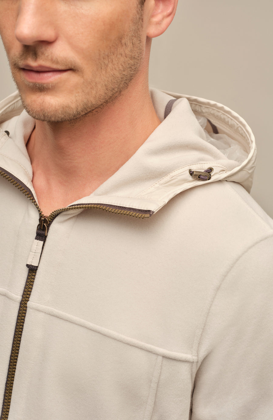 Detailansicht der Herrenjacke "Thomas" von einem Model getragen in der Farbe Sandstone. Die Jacke zeichnet sich durch einen minimalistischen Schnitt, einen verstellbaren Nylon-Kapuzenkragen und praktische Reißverschlusstaschen aus. Ideal für alle Jahreszeiten, kombiniert sie Funktionalität mit modernem Design