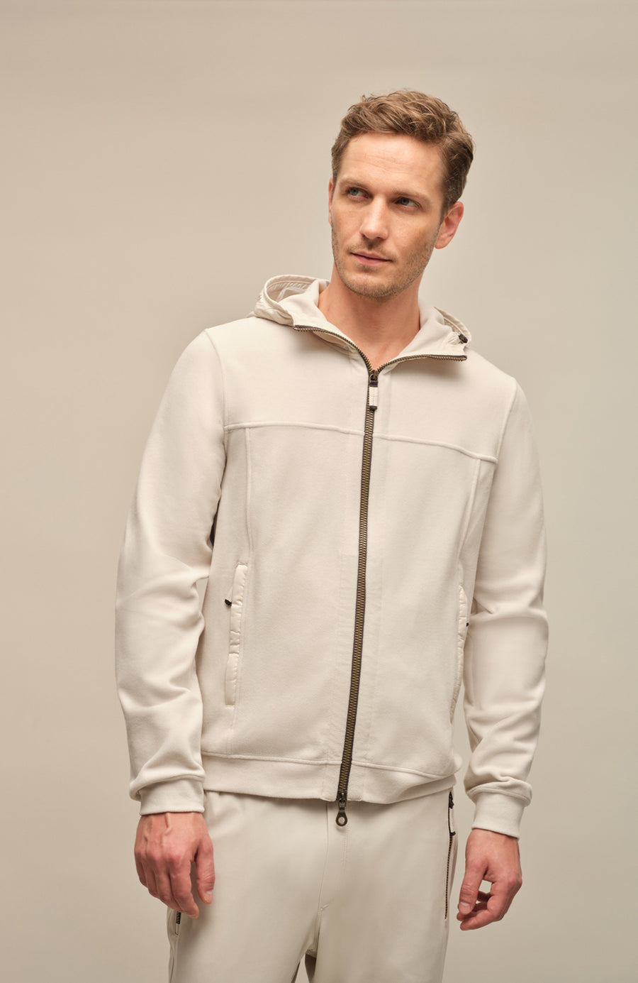 Vorderansicht der Herrenjacke "Thomas" von einem Model getragen, in der Farbe weiß. Die Jacke besteht aus umweltfreundlichem Biodegradable Fleece und zeichnet sich durch einen sportlichen Schnitt, einen verstellbaren Nylon-Kapuzenkragen und praktische Reißverschlusstaschen aus. Ideal für alle Jahreszeiten, kombiniert sie Funktionalität mit modernem Design