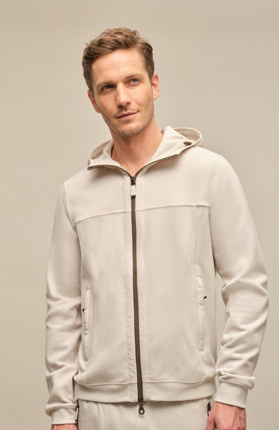 Vorderansicht der Herrenjacke "Thomas" von einem Model getragen, in der Farbe weiß. Die Jacke besteht aus umweltfreundlichem Biodegradable Fleece und zeichnet sich durch einen sportlichen Schnitt, einen verstellbaren Nylon-Kapuzenkragen und praktische Reißverschlusstaschen aus. Ideal für alle Jahreszeiten, kombiniert sie Funktionalität mit modernem Design