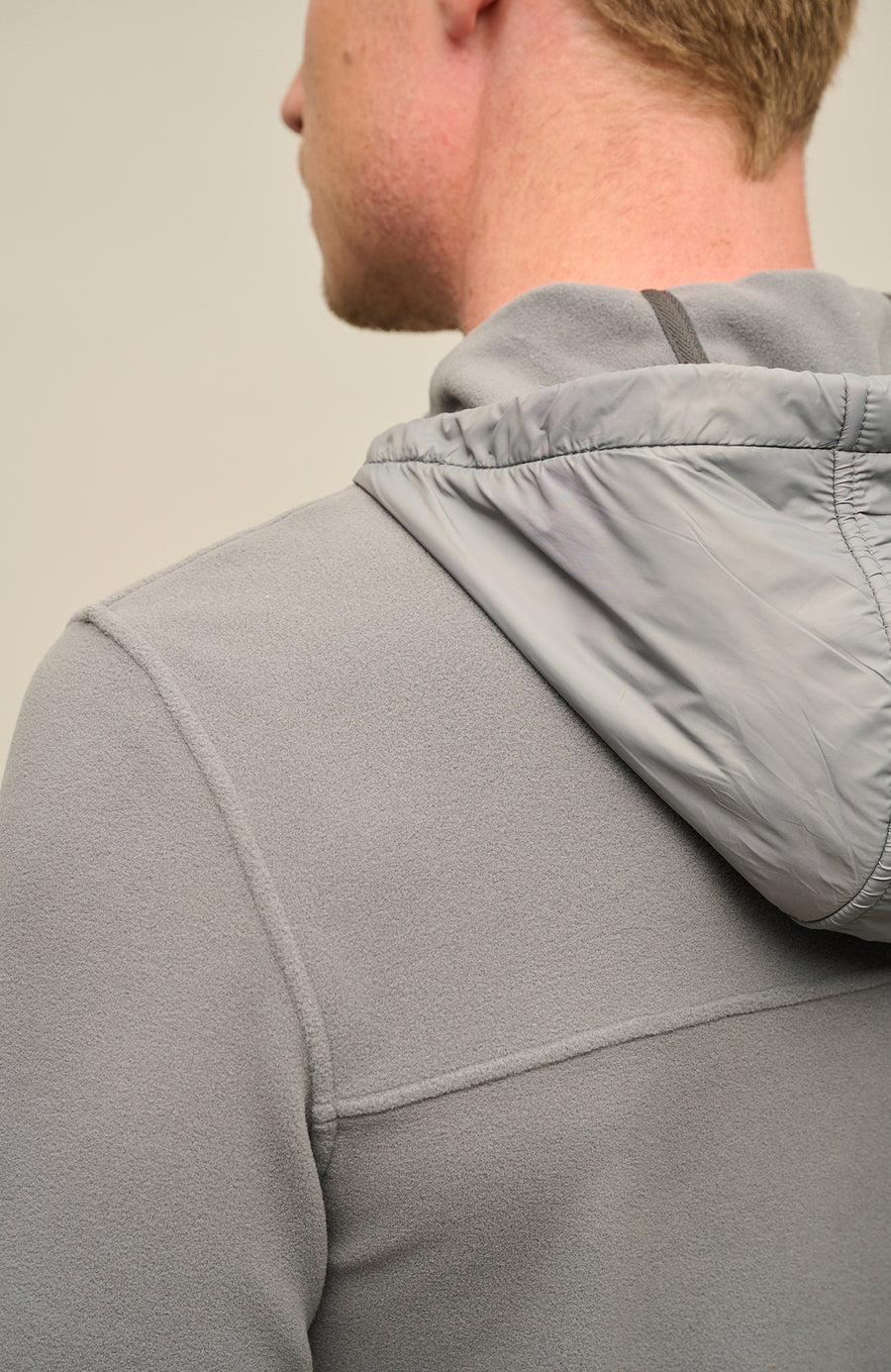 Detailansicht der Herrenjacke "Thomas" von einem Model getragen in der Farbe grau. Die Jacke zeichnet sich durch einen minimalistischen Schnitt, einen verstellbaren Nylon-Kapuzenkragen und praktische Reißverschlusstaschen aus. Ideal für alle Jahreszeiten, kombiniert sie Funktionalität mit modernem Design