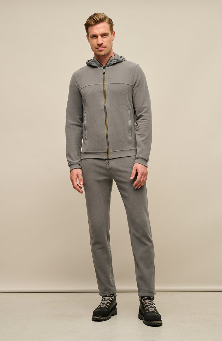 Vorderansicht der Herrenjacke "Thomas" von einem Model getragen, in der Farbe grau. Die Jacke besteht aus umweltfreundlichem Biodegradable Fleece und zeichnet sich durch einen sportlichen Schnitt, einen verstellbaren Nylon-Kapuzenkragen und praktische Reißverschlusstaschen aus. Ideal für alle Jahreszeiten, kombiniert sie Funktionalität mit modernem Design