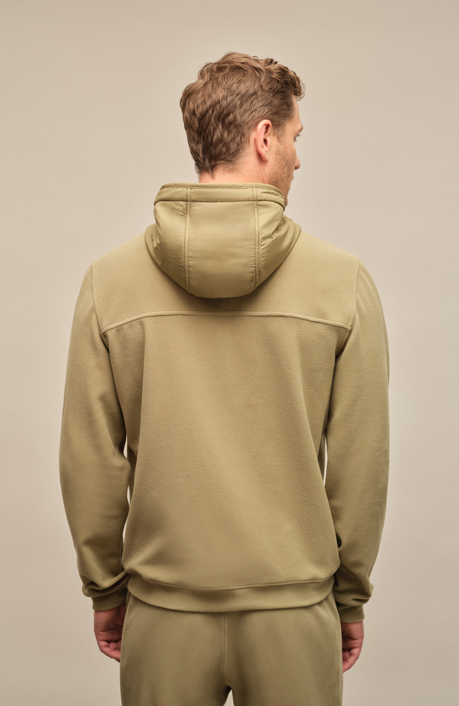 Rückansicht der Herrenjacke "Thomas" von einem Model getragen, in der Farbe grün. Die Jacke zeichnet sich durch einen minimalistischen Schnitt, einen verstellbaren Nylon-Kapuzenkragen und praktische Reißverschlusstaschen aus. Ideal für alle Jahreszeiten, kombiniert sie Funktionalität mit modernem Design