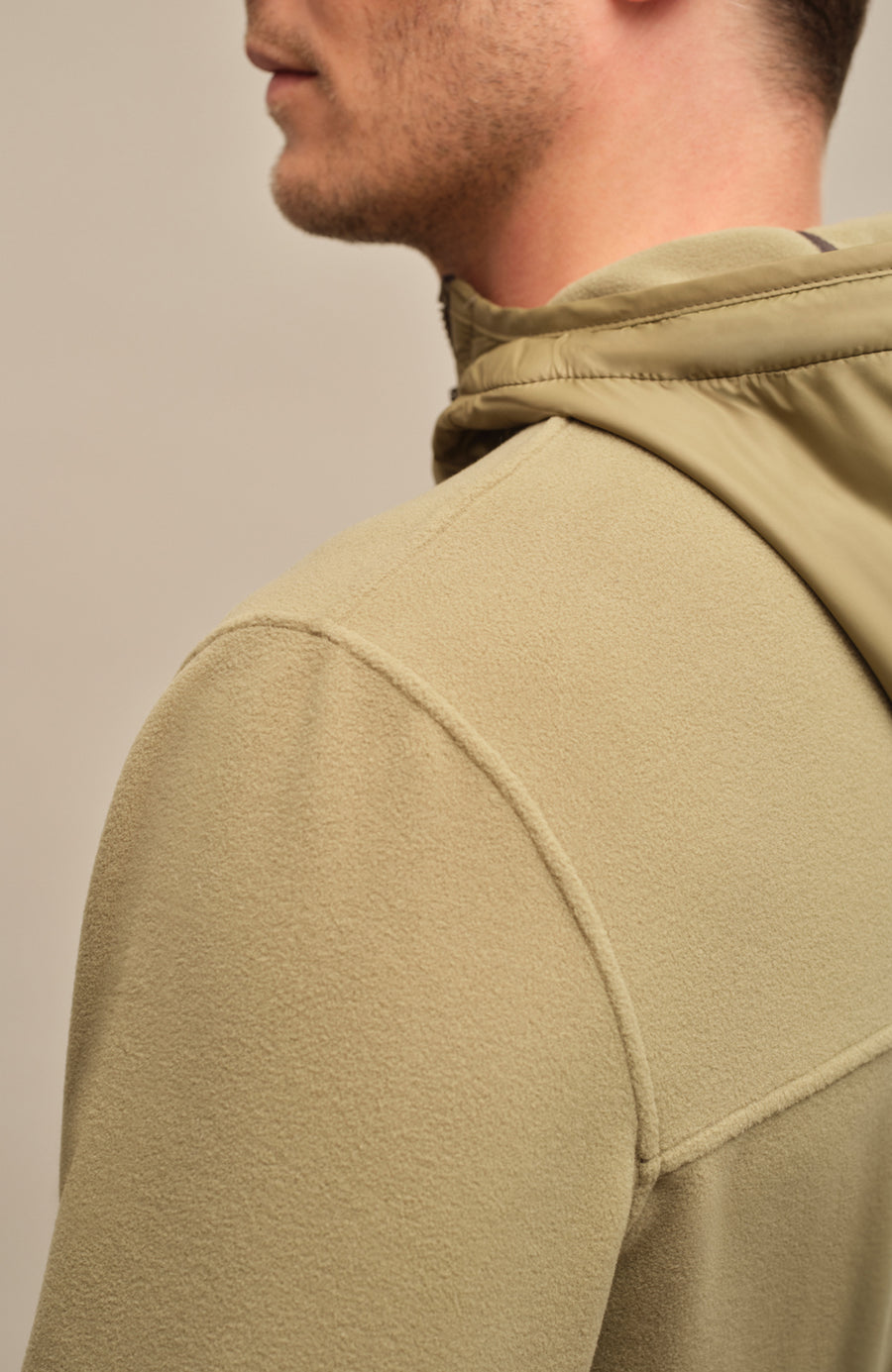 Detailansicht der Herrenjacke "Thomas" von einem Mode getragen in der Farbe grün. Die Jacke zeichnet sich durch einen minimalistischen Schnitt, einen verstellbaren Nylon-Kapuzenkragen und praktische Reißverschlusstaschen aus. Ideal für alle Jahreszeiten, kombiniert sie Funktionalität mit modernem Design