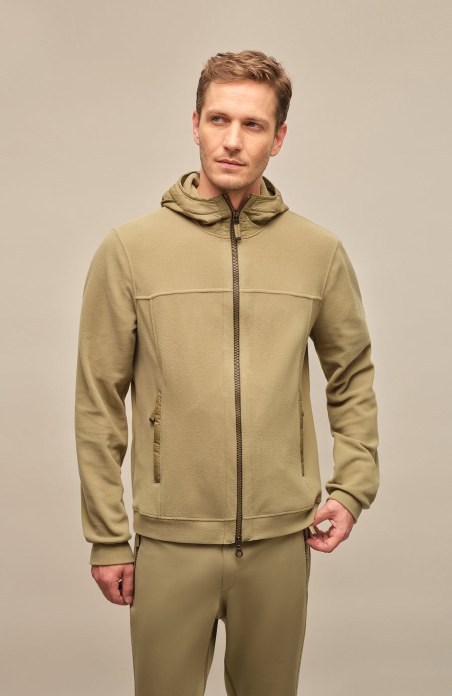 Vorderansicht der Herrenjacke "Thomas" von einem Model getragen, in der Farbe grün. Die Jacke besteht aus umweltfreundlichem Biodegradable Fleece und zeichnet sich durch einen sportlichen Schnitt, einen verstellbaren Nylon-Kapuzenkragen und praktische Reißverschlusstaschen aus. Ideal für alle Jahreszeiten, kombiniert sie Funktionalität mit modernem Design