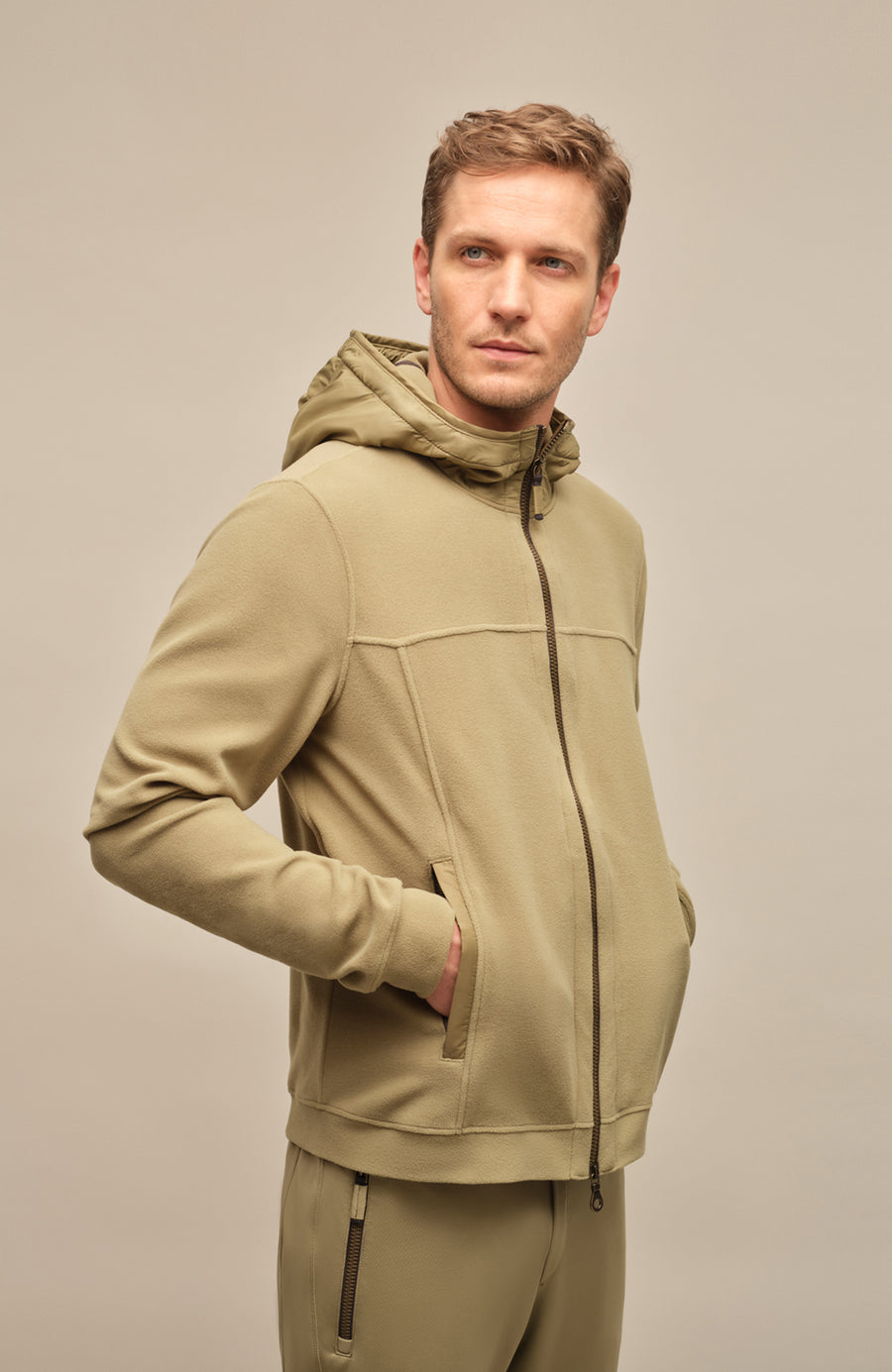 Seitenansicht der Herrenjacke "Thomas" von einem Model getragen, in der Farbe grün. Die Jacke besteht aus umweltfreundlichem Biodegradable Fleece und zeichnet sich durch einen sportlichen Schnitt, einen verstellbaren Nylon-Kapuzenkragen und praktische Reißverschlusstaschen aus. Ideal für alle Jahreszeiten, kombiniert sie Funktionalität mit modernem Design