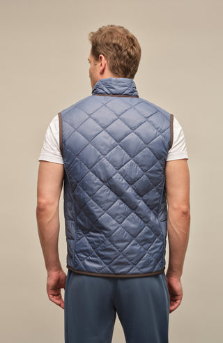 Rückansicht eines Herrenmodels mit der gesteppten Weste „Henri-QL“ von Frauenschuh in denimblau; hochwertige Nylon-Qualität mit feiner Rautensteppung, sichtbar über die gesamte Rückenfläche; sportlich-taillierte Passform betont Schultern und Rücken; dezente Nahtführung für ein klares, modernes Design; ideal für die Übergangszeit Frühling und Sommer; das Model steht mit dem Rücken zur Kamera und trägt die Weste über einem leichten Oberteil – stilvolle Kombination aus Funktionalität und Luxusmode