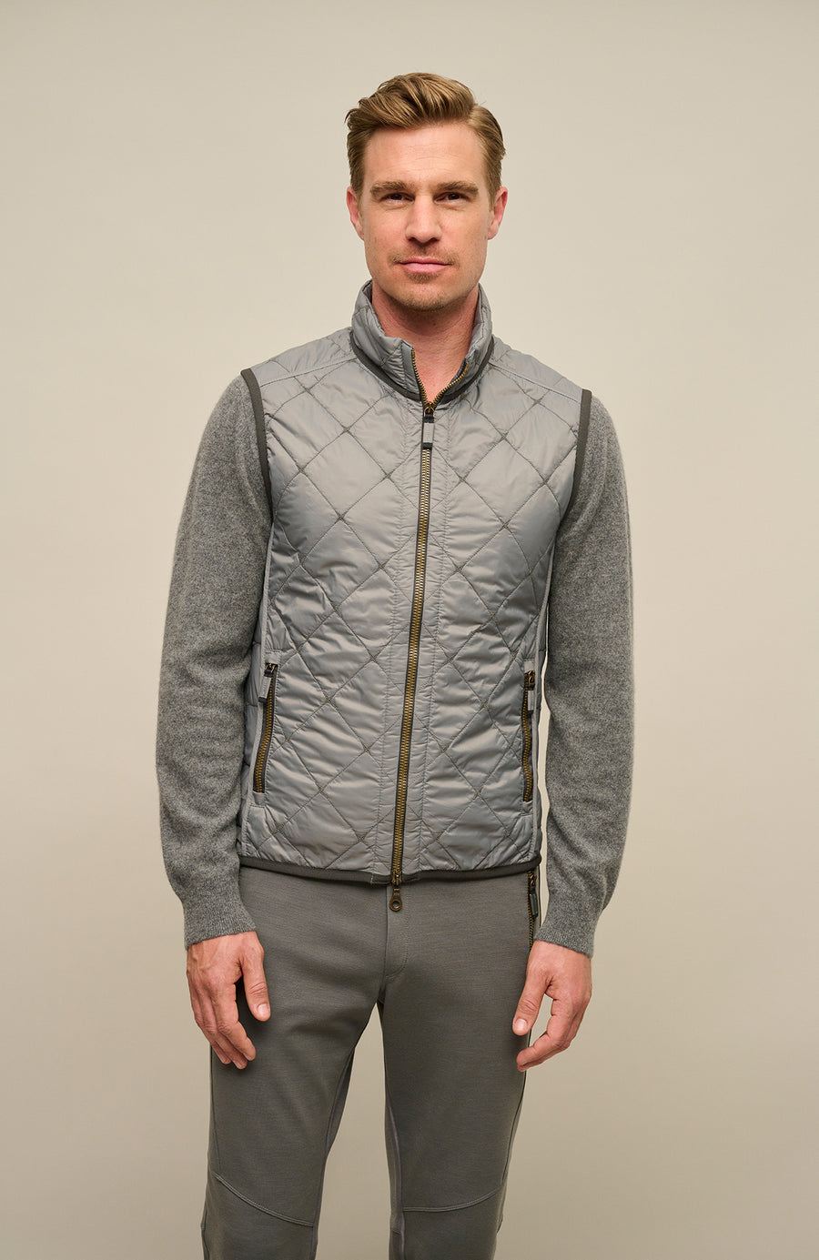 Model trägt die Damen-Quiltweste „Henri-QL“ von Frauenschuh in Cement (Grau); elegante, rautenförmig gesteppte Weste aus leichtem, hochwertigem Nylonmaterial; taillierte Passform für eine feminine Silhouette; ausgestattet mit einem sportlich-eleganten Stehkragen und Zwei-Wege-Reißverschluss; ideal für Übergangszeiten wie Frühling und Sommer; das Model steht frontal zur Kamera und präsentiert die moderne, funktionale Outdoor-Weste