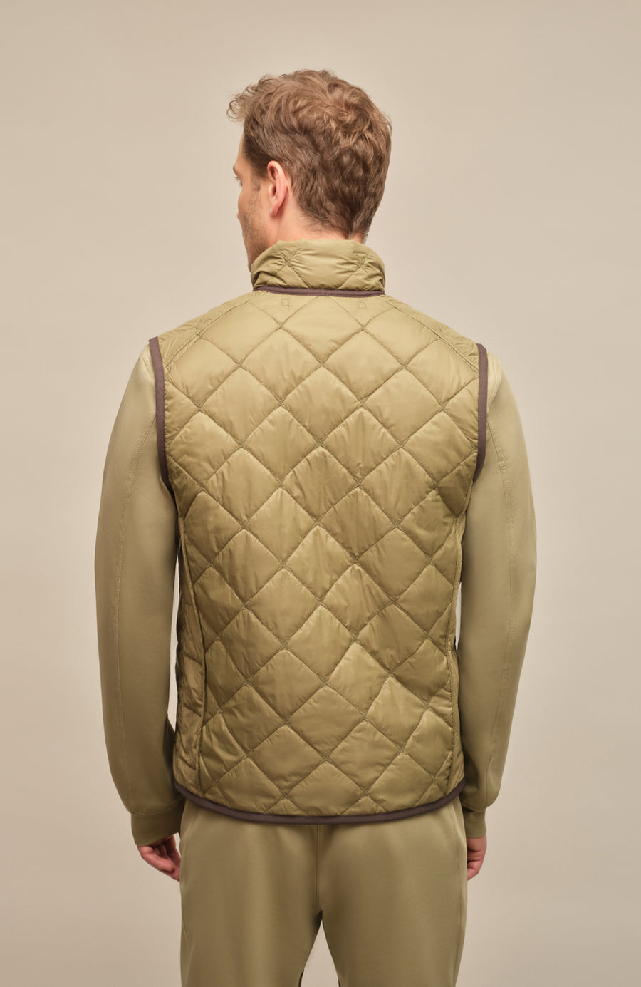 Rückansicht eines Herrenmodels mit der gesteppten Weste „Henri-QL“ von Frauenschuh in Sage (Grün); hochwertige Nylon-Qualität mit feiner Rautensteppung, sichtbar über die gesamte Rückenfläche; sportlich-taillierte Passform betont Schultern und Rücken; dezente Nahtführung für ein klares, modernes Design; ideal für die Übergangszeit Frühling und Sommer; das Model steht mit dem Rücken zur Kamera und trägt die Weste über einem leichten Oberteil – stilvolle Kombination aus Funktionalität und Luxusmode