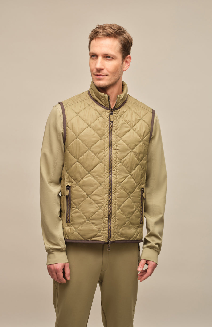 Model trägt die Damen-Quiltweste „Henri-QL“ von Frauenschuh in Sage (Grün); elegante, rautenförmig gesteppte Weste aus leichtem, hochwertigem Nylonmaterial; taillierte Passform für eine feminine Silhouette; ausgestattet mit einem sportlich-eleganten Stehkragen und Zwei-Wege-Reißverschluss; ideal für Übergangszeiten wie Frühling und Sommer; das Model steht frontal zur Kamera und präsentiert die moderne, funktionale Outdoor-Weste