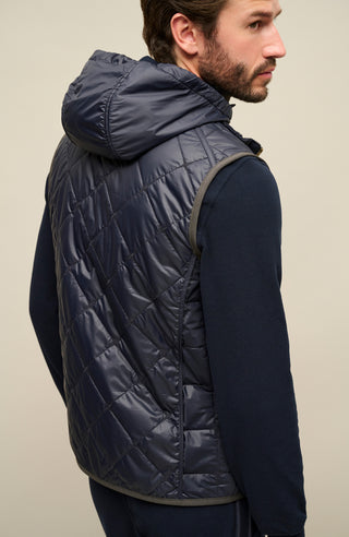 Rückansicht eines Herrenmodels mit der gesteppten Weste „Henri-QL“ von Frauenschuh in Midnight (dunkelblau); hochwertige Nylon-Qualität mit feiner Rautensteppung, sichtbar über die gesamte Rückenfläche; sportlich-taillierte Passform betont Schultern und Rücken; dezente Nahtführung für ein klares, modernes Design; ideal für die Übergangszeit Frühling und Sommer; das Model steht mit dem Rücken zur Kamera und trägt die Weste über einem leichten Oberteil – stilvolle Kombination aus Funktionalität und Luxusmode
