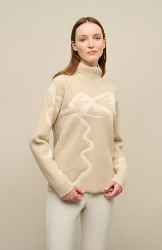 Modelvorderansicht eines Damenpullovers aus 100 % extrafeiner Merinowolle, Modell „Chatel-ME“ in der Farbe Beige. Die Vorderseite zeigt ein kunstvoll gestaltetes Jacquard-Motiv aus skizzierten Berglandschaften, urbanen Elementen und dynamischen Skifahrern. Das hochwertige Merinogarn – leicht, weich und angenehm auf der Haut – wird in Italien produziert und auf modernsten Maschinen verarbeitet. Die Kombination aus künstlerischem Design & technischer Strickkunst macht den Pullover besonders stilvoll