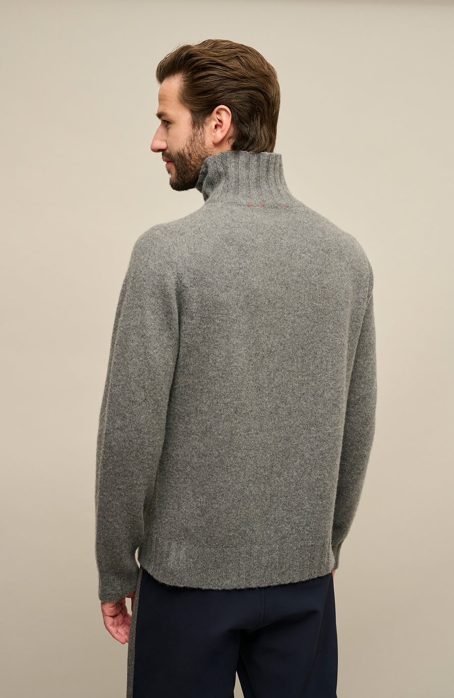 Rückansicht-Bild eines Herrenpullovers aus 100 % Kaschmir von Frauenschuh, Modell „Aiden 2.0“ (Artikelnummer WS_131-0) in der Farbe Grau. Der edle Cashmere-Strickpullover wird von einem männlichen Model getragen und zeigt auf der Rückseite eine klare, puristische Linienführung mit fein gestricktem Rumpf und kontrastierenden Rippenbündchen an Ärmelenden und Saum. Der schmale Stehkragen schmiegt sich elegant an den Nacken an und unterstreicht das sportlich-elegante Design.