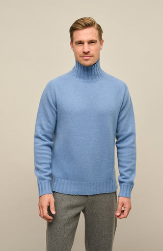 Ein Model trägt einen hochwertigen Herrenpullovers aus reinem Kaschmir von Frauenschuh, Modell „Aiden 2.0“ (Artikelnummer Aiden-WS_209-0), Farbe Denim. Der luxuriöse Strickpullover für Herbst und Winter verfügt über einen eleganten, schmalen Stehkragen und ist aus feinstem Cashmere gefertigt. Die Ärmelabschlüsse, der Kragen und der untere Abschluss sind in feiner Rippenstruktur gestrickt und setzen sich optisch und haptisch vom glatt gestrickten Körper ab. Ein stilvolles, sportlich-elegantes Basic.