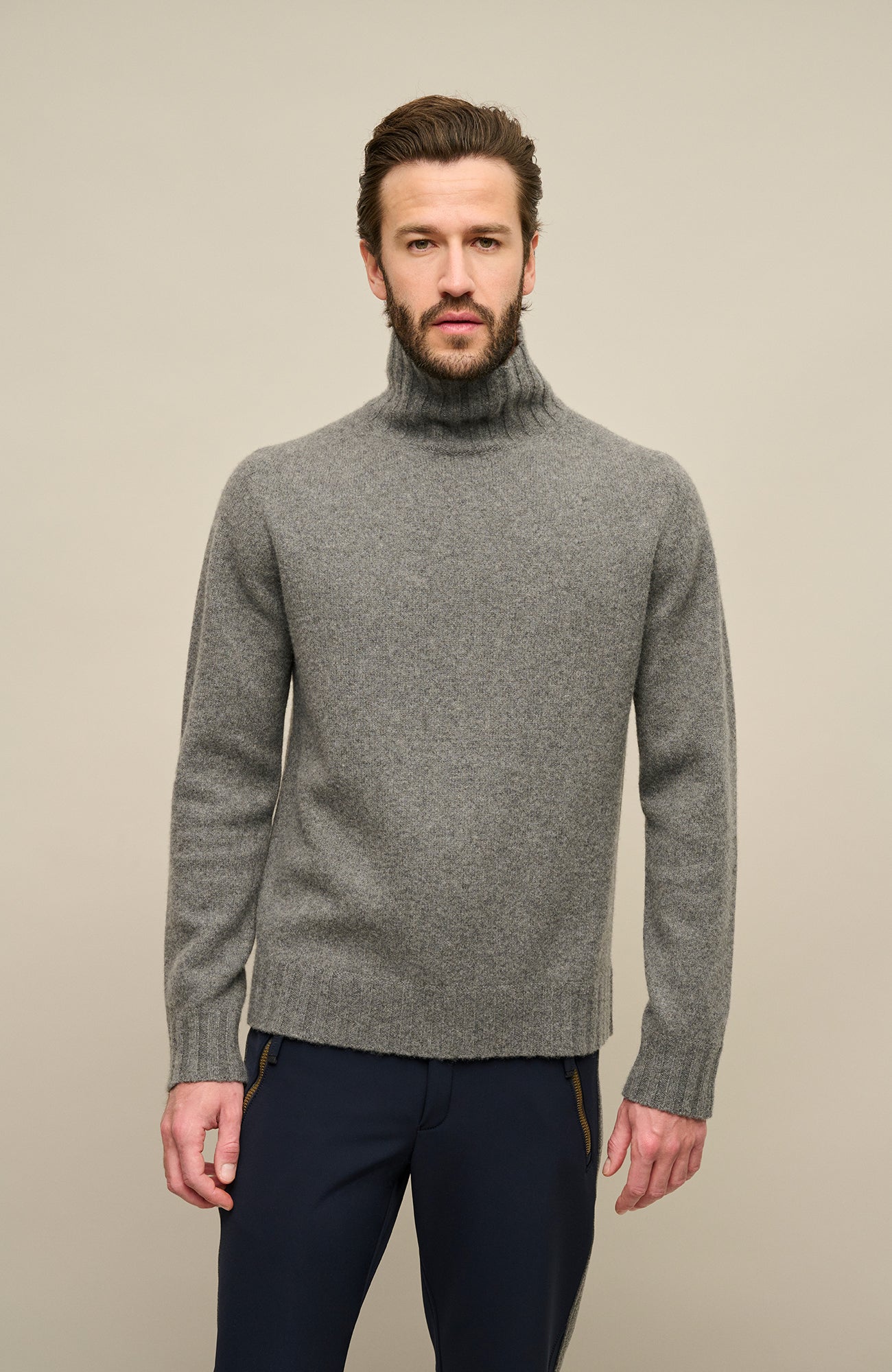 Ein Model trägt einen hochwertigen Herrenpullovers aus reinem Kaschmir von Frauenschuh, Modell „Aiden 2.0“ (Artikelnummer Aiden-WS_131-0), Farbe Grau. Der luxuriöse Strickpullover für Herbst und Winter verfügt über einen eleganten, schmalen Stehkragen und ist aus feinstem Cashmere gefertigt. Die Ärmelabschlüsse, der Kragen und der untere Abschluss sind in feiner Rippenstruktur gestrickt und setzen sich optisch und haptisch vom glatt gestrickten Körper ab. Ein stilvolles, sportlich-elegantes Basic.