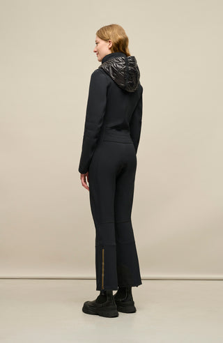 Damen-Skioverall GWEN-S in Schwarz von FRAUENSCHUH – figurbetonter Funktionsoverall in hochwertiger Ausführung, getragen von einem Model – Seitenansicht mit taillierter Silhouette und sportlich-elegantem Schnitt – körpernahes Design mit ergonomischer Linienführung, perfekt für Outdoor-Aktivitäten und Wintersport – atmungsaktiv, elastisch, wasserabweisend. Am unteren Bein seitlich mit Reißverschluss für einfaches An- und Ausziehen