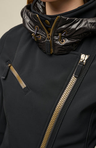 FRAUENSCHUH Damen-Funktionsjacke Gwen-S in Schwarz – Detailansicht des asymmetrischen, goldfarbenen Reißverschlusses und der verschließbaren Brusttasche – Stehkragen mit glänzendem, wattiertem Material, verschließbar durch Druckknöpfe. Mit Kapuze, verstellbar durch Kordelzug mit Metallösen, verschließbar mit einem Reißverschluss – hochwertiges Material mit klarer Nahtführung, perfekt für Outdoor und Wintersport – modernes, funktionales Design aus Österreich, gefertigt für optimale Passform und Schutz