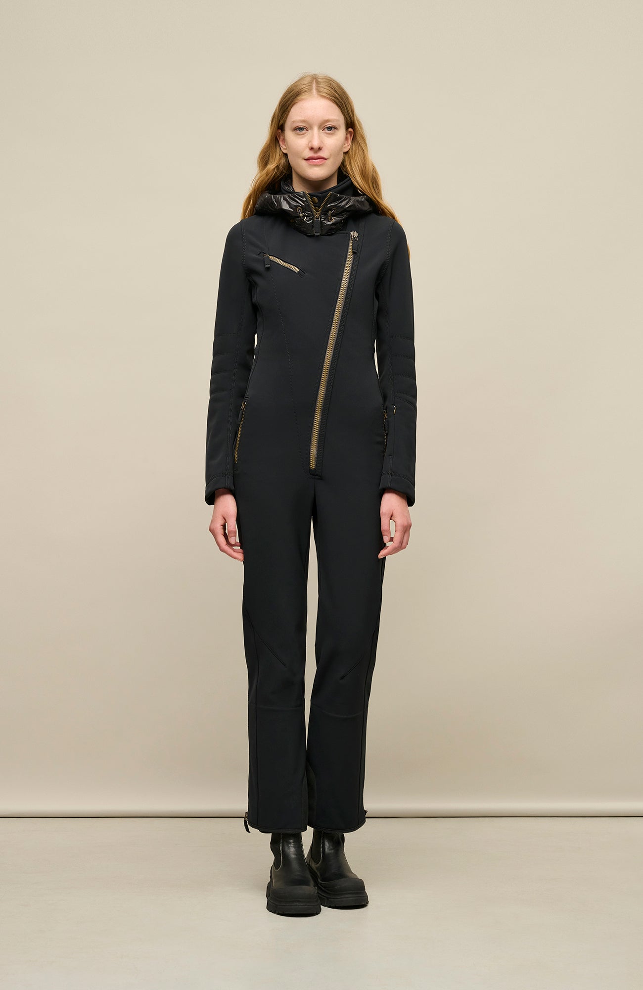 Model zeigt die Vorderansicht des Damen-Skioverall GWEN-S in Schwarz – eleganter, figurbetonter Catsuit aus elastischem Funktionsmaterial mit hohem Tragekomfort – ideal für Wintersport, Skifahren und stylische Outdoor-Aktivitäten – wasserabweisend, atmungsaktiv und winddicht – körpernahe Passform mit durchgehendem leicht schräg verlaufendem Reißverschluss, hoher Kragen, Kapuze und taillierter Schnitt. Außerdem gibt es eine Brusttasche – edle Verarbeitung in typisch minimalistischer FRAUENSCHUH-Ästhetik