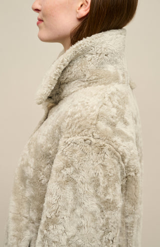 Damen Lammfellcape Modell Dolli in der Farbe savanna Modelansicht seitlich – edles Cape aus weichem Lammfell mit fließendem Schnitt, stilvoll und wärmend für die kalte Jahreszeit.“