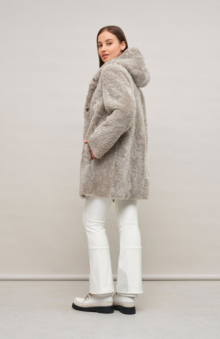 „Damen Lammfellmantel mit Kapuze von Frauenschuh, Modell Olivera in der Farbe Savanna, Model Rueckansicht – luxuriöser Wintermantel aus hochwertigem Lammfell für stilvolle Wärme.