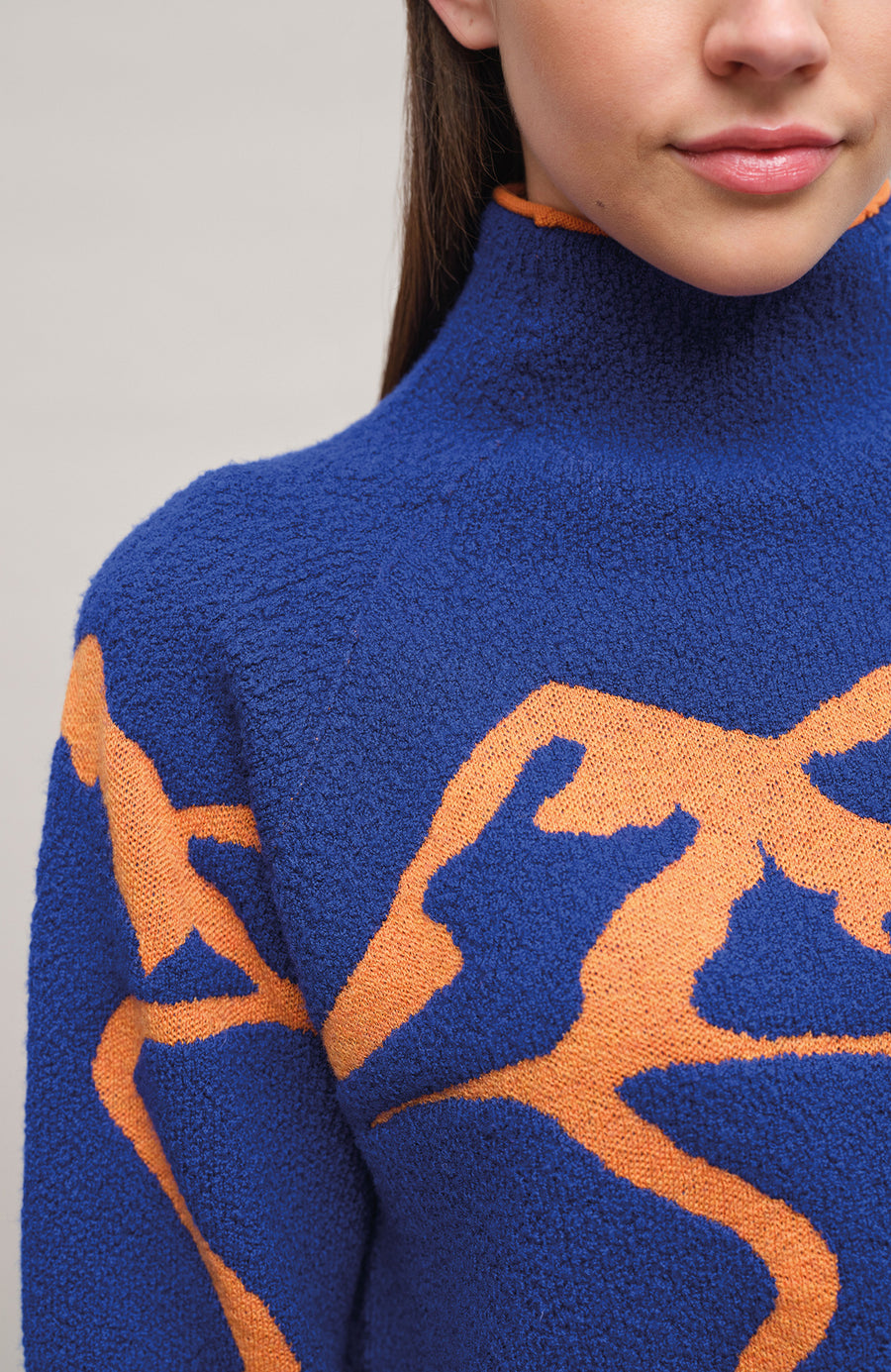 Detailansicht am Model eines Damenpullovers aus 100 % extrafeiner Merinowolle, Modell „Chatel-ME“ in der Farbe Marineblau. Die Vorderseite zeigt ein kunstvoll gestaltetes Jacquard-Motiv aus skizzierten Berglandschaften, urbanen Elementen und dynamischen Skifahrern. Das hochwertige Merinogarn – leicht, weich und angenehm auf der Haut – wird in Italien produziert und auf modernsten Maschinen verarbeitet. Die Kombination aus künstlerischem Design & technischer Strickkunst macht den Pullover besonders stilvoll