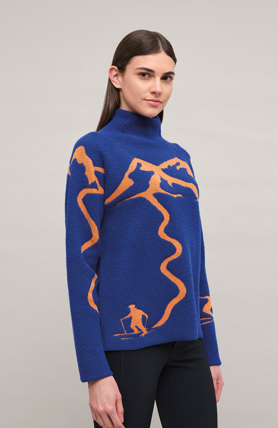 Vorderansicht am Model eines Damenpullovers aus 100 % extrafeiner Merinowolle, Modell „Chatel-ME“ in der Farbe Marineblau. Die Vorderseite zeigt ein kunstvoll gestaltetes Jacquard-Motiv aus skizzierten Berglandschaften, urbanen Elementen und dynamischen Skifahrern. Das hochwertige Merinogarn – leicht, weich und angenehm auf der Haut – wird in Italien produziert und auf modernsten Maschinen verarbeitet. Die Kombination aus künstlerischem Design & technischer Strickkunst macht den Pullover besonders stilvoll
