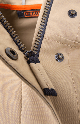 Damen-Knielanger Mantel aus Outdoor Cotton, wasser- und windabweisend, gerade Passform mit schmaler Silhouette, Stehkragen und weitenregulierbare Kapuze, Knopfleiste mit verdecktem Zwei-Wege-Zipper, Ripsband an Ärmelabschlüssen und Saum, seitliche Taschen mit markantem Zipper. In der Farbe Beige-Braun (Farbe: caramel).