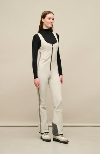 Ski-Catsuit Davina2.0-S im Latzhosen-Stil ohne Ärmel, schmaler figurbetonter Schnitt mit ausgestelltem Bein, femininer Bustier-Ausschnitt, Streifen an den Beinaußenseiten aus Alcantara-Leder, Träger hinten aus elastischem Gummi, ergonomisches Knie, markanter langer Zipper, auffallende Nähte, Seitentaschen mit Zip, Kantenschutz aus Alcantara-Leder und Schneefang. Enganliegend, feminin, betont Silhouette und Bewegungsfreiheit. In der Farbe Weiß-Beige (Farbe: sandstone)