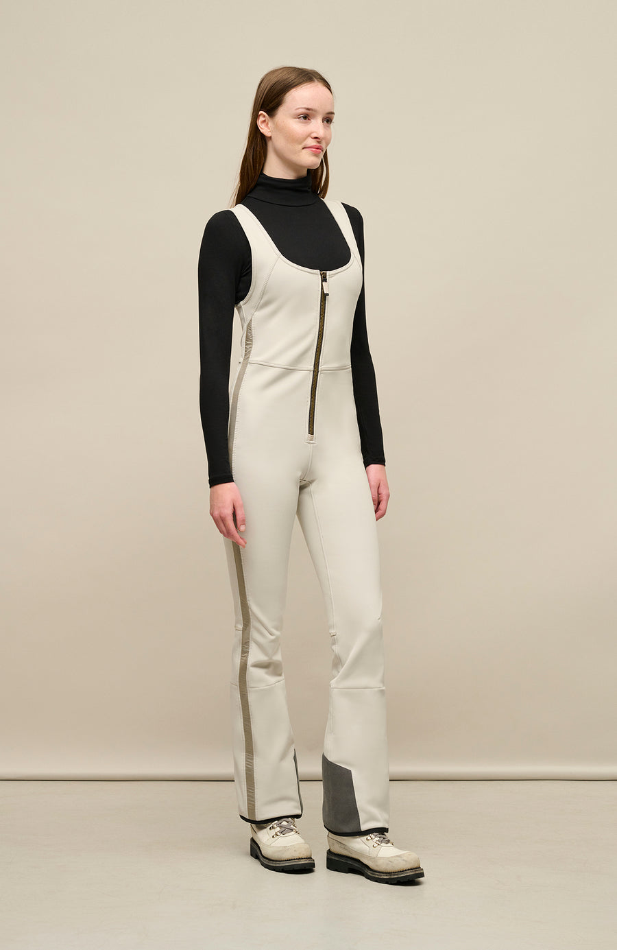 Ski-Catsuit Davina2.0-S im Latzhosen-Stil ohne Ärmel, schmaler figurbetonter Schnitt mit ausgestelltem Bein, femininer Bustier-Ausschnitt, Streifen an den Beinaußenseiten aus Alcantara-Leder, Träger hinten aus elastischem Gummi, ergonomisches Knie, markanter langer Zipper, auffallende Nähte, Seitentaschen mit Zip, Kantenschutz aus Alcantara-Leder und Schneefang. Enganliegend, feminin, betont Silhouette und Bewegungsfreiheit. In der Farbe Weiß-Beige (Farbe: sandstone)